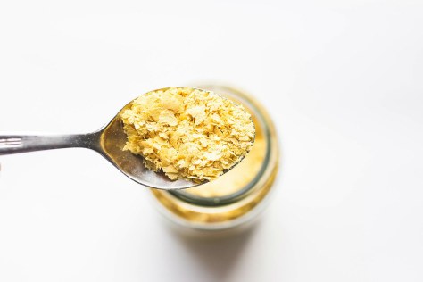 Spoon of vegan nutritional yeast flakes on white background